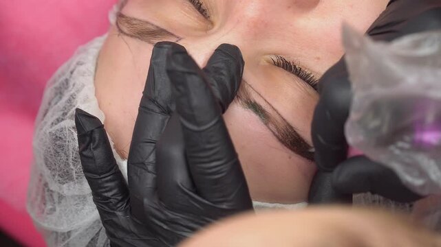 Makeup artist plucks eyebrows and doing eyebrow permanent makeup correction in a beauty salon. Concept makeup and cosmetology skin care.