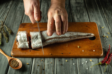 Hands skillfully slice a fresh fish on a wooden cutting board adorned with aromatic spices. The...