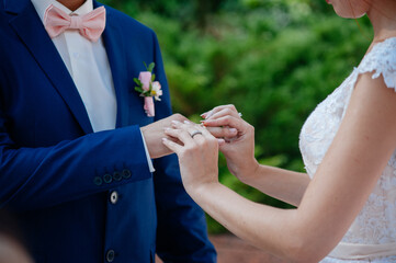 Fototapeta premium Close-up of the bride placing the wedding ring on the groom's finger during their wedding ceremony outdoors.