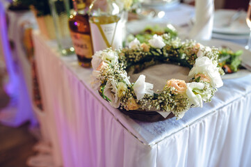 A delicate wedding floral crown with white and pink flowers on a table surrounded by alcohol...