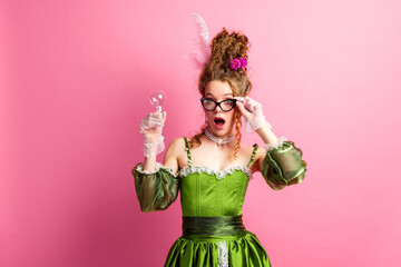 Young woman in green vintage gown holding a light bulb against pink background, blending past and modern creativity
