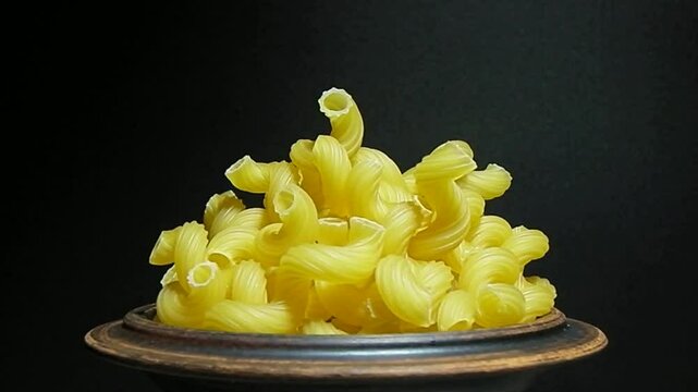 raw pasta in the shape of twisted horns (Stortelli), rotating on a black background