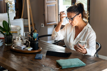 Businesswoman working from home feeling stressed reading bad news on mobile phone