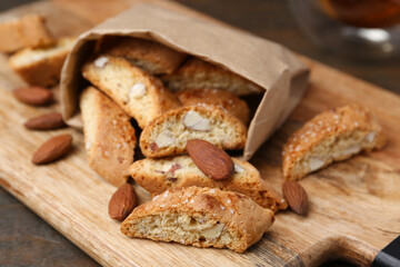 Paper bag with tasty almond biscuits (Cantuccini) and nuts on wooden table, closeup