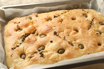 Delicious focaccia bread with olives and thyme in baking dish on table, closeup