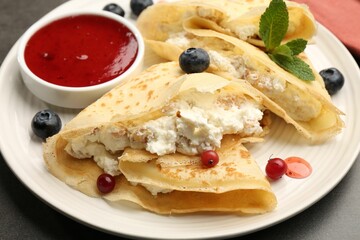 Delicious crepes with cottage cheese, jam, redcurrants and blueberries on grey table, closeup