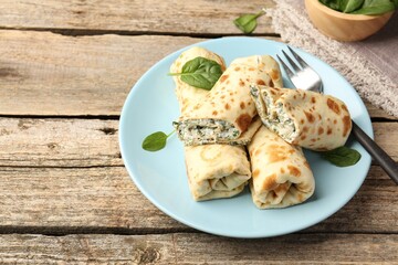 Tasty rolled crepes with cottage cheese and spinach served on wooden table, closeup. Space for text