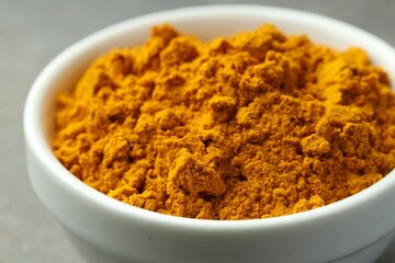Turmeric powder in bowl on grey table, closeup