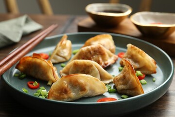 Delicious fried gyoza dumplings with green onions and chili peppers served on wooden table, closeup