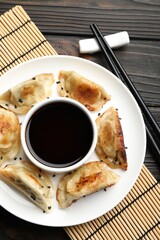 Delicious fried gyoza dumplings with sesame seeds served on wooden table, top view
