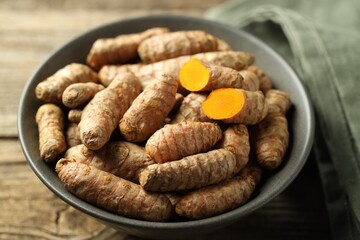 Tumeric rhizomes in bowl on wooden table, closeup