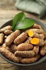 Tumeric rhizomes with leaves in bowl on wooden table, closeup