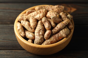Tumeric rhizomes in bowl on wooden table, closeup