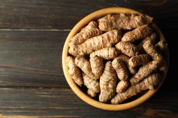 Tumeric rhizomes in bowl on wooden table, top view. Space for text