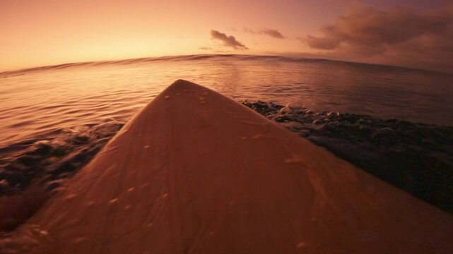 Surfer rowing on surfboard and duck dive under waves in ocean. First-person view and crashing waves with bright sunset