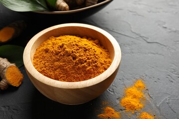 Aromatic turmeric powder in bowl and fresh roots on black table, closeup. Space for text
