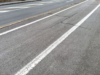 Urban road with cracks and faded white lines on asphalt surface