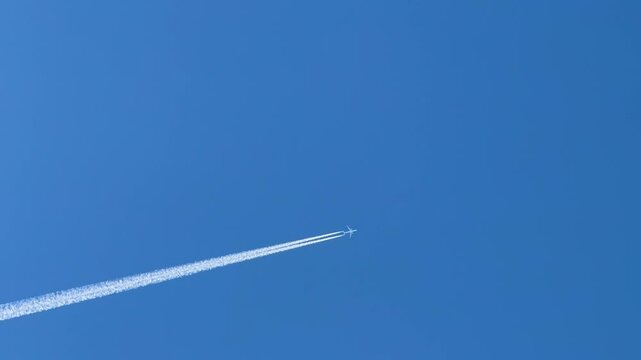 A jet plane creates a white trail across the blue sky, forming a striking geometric pattern as it flies.