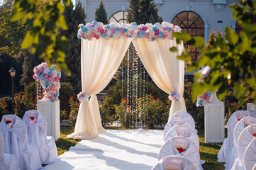 A romantic outdoor wedding ceremony setup with a floral arch, decorated chairs, and a beautiful garden backdrop.
