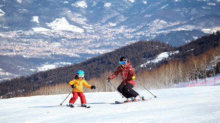 A mother guiding her daughter in learning how to ski as they glide down a slope on a bright and sunny winter holiday in El Tarter, Andorra, nestled in the Pyrenees Mountains