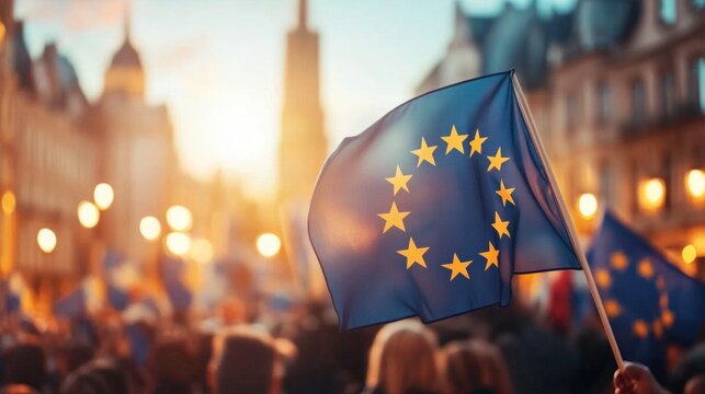 A European flag held high amidst a crowd, bathed in the warm glow of sunset.