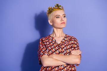 Confident young woman wearing a crown and stylish printed shirt posing against a vibrant purple...