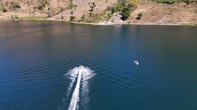Vista panor&aacute;mica de lago profundo entre monta&ntilde;as con lancha r&aacute;pida dejando estela