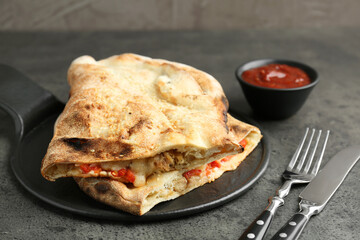 Halves of tasty calzone with meat, cheese, tomato and sauce on grey textured table, closeup
