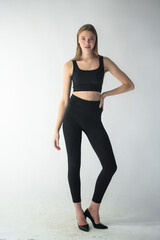 professional model in a sleek black outfit adjusts her jeans while gazing off-camera, showcasing...