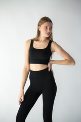 professional model in a sleek black outfit adjusts her jeans while gazing off-camera, showcasing...