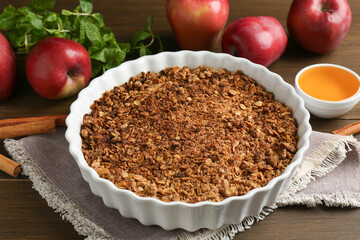 Tasty apple crisp in baking dish and ingredients on wooden table, closeup