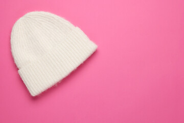 Warm woolen hat on pink background, top view. Space for text