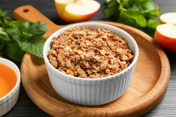 Delicious apple crisp in bowl and ingredients on black table, closeup