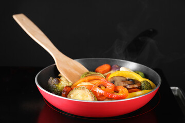 Frying pan with vegetables and mushrooms on stove, closeup