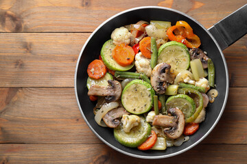 Different vegetables and mushrooms in frying pan on wooden table, top view
