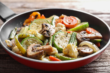 Different vegetables and mushrooms in frying pan on wooden table, closeup