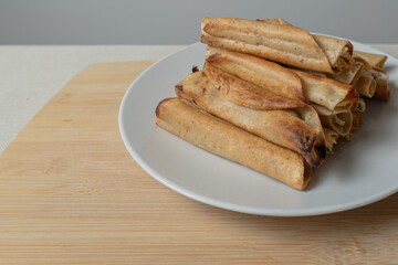 Golden tacos prepared on a white plate and wooden board