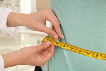 Nutritionist measuring overweight woman's waist with tape in hospital, closeup