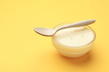 Tasty condensed milk in bowl and spoon on orange background, closeup. Space for text