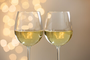 Tasty white wine in glasses against grey background with blurred lights, closeup. Bokeh effect