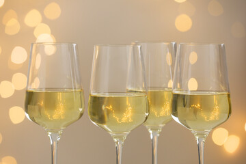 Tasty white wine in glasses against grey background with blurred lights, closeup. Bokeh effect