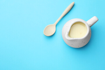 Tasty condensed milk in jug and spoon on light blue background, top view. Space for text