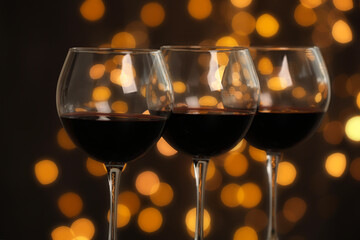 Tasty red wine in glasses against dark background with blurred lights, closeup. Bokeh effect