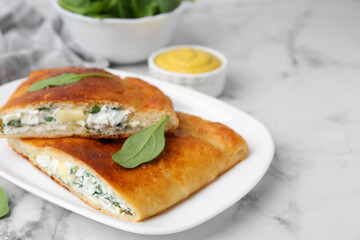 Pieces of tasty calzone with basil, cheese and sauce on white marble table, closeup. Space for text