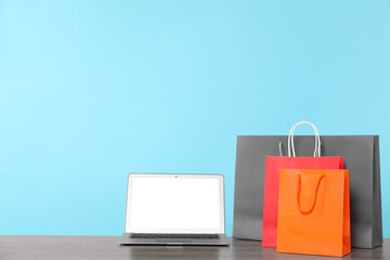 Internet shopping. Laptop and colorful paper bags on wooden table against light blue background