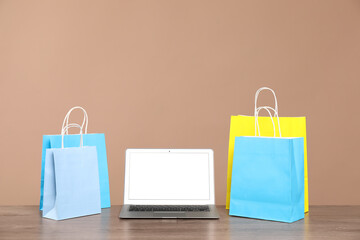 Internet shopping. Laptop and colorful paper bags on wooden table against brown background