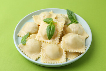 Delicious ravioli with cheese and basil on green background, closeup