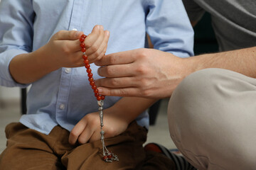 Muslim man and his son with prayer beads at home, closeup