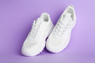 Pair of stylish white sneakers on violet background