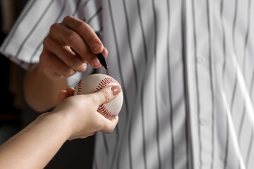 Sportsman signing autograph on baseball ball against black background, closeup